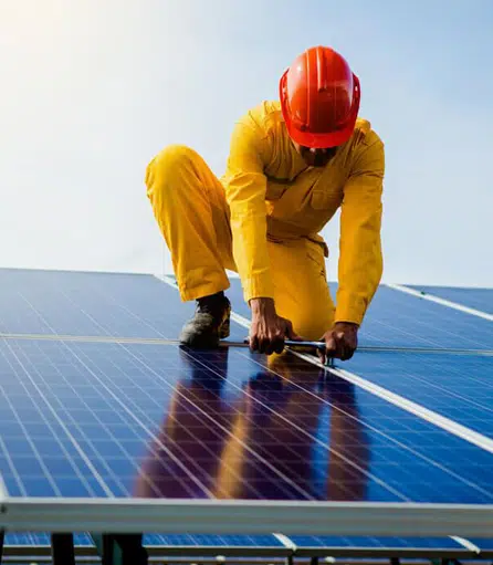 Worker installing solar panels on a roof, wearing safety gear.