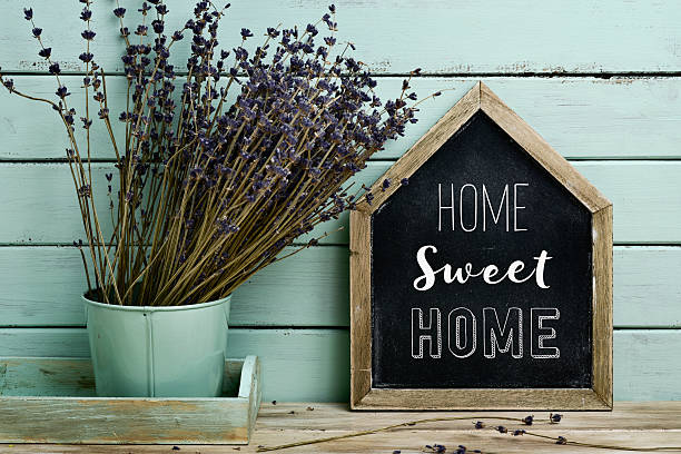 house-shaped chalkboard with the text home sweet home written in it and a bunch of lavender flowers in a flower pot, against a rustic pale blue background.